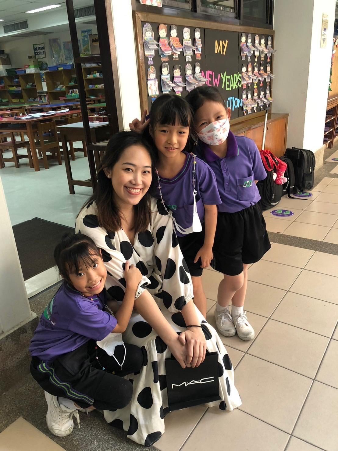 Kru Ice smiling with three of her young students in a school library